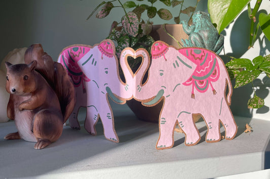 Decorative elephant figurines with pink and purple patterns on a shelf with plants in the background.