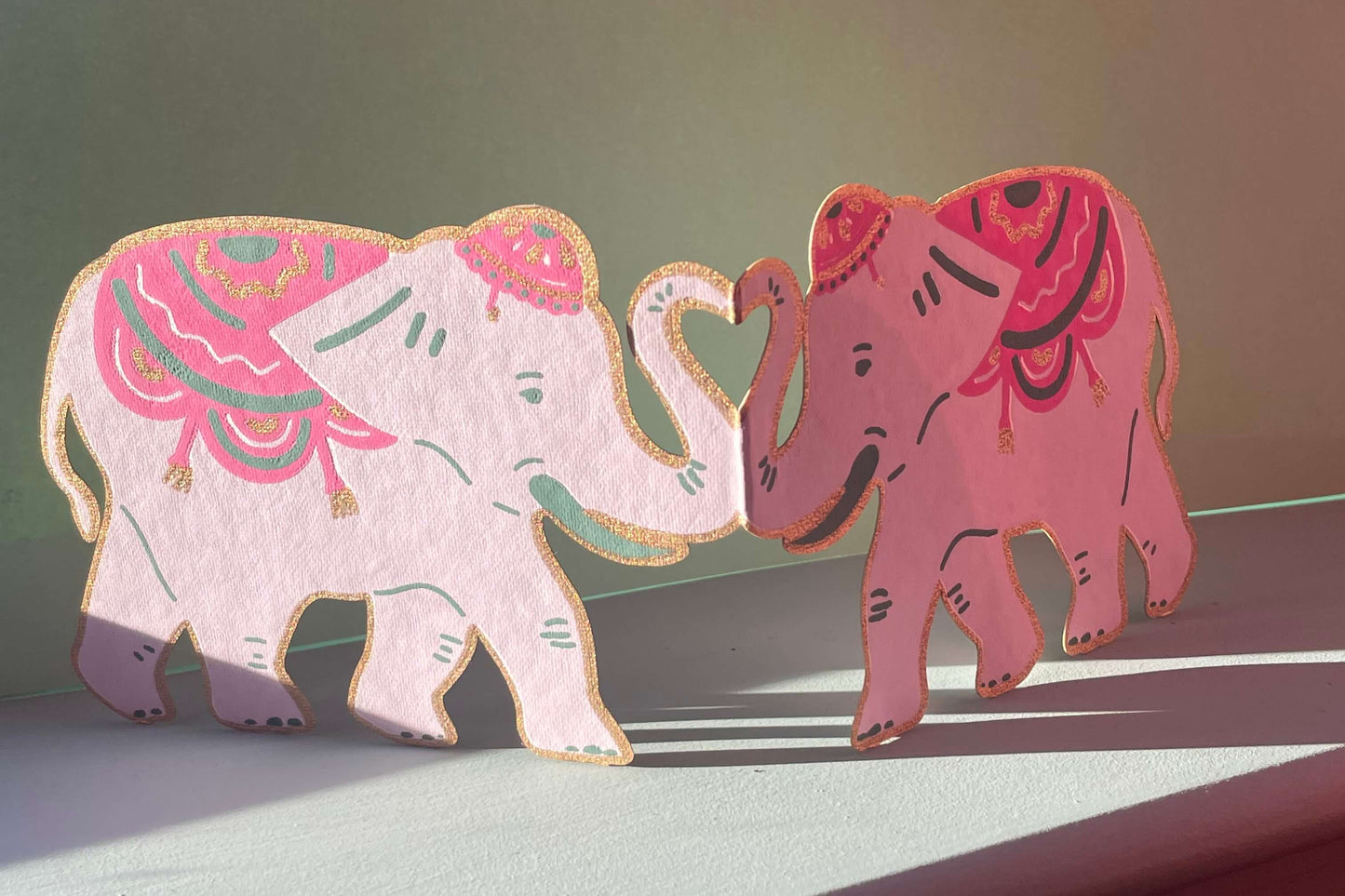 Two decorative elephants with pink and white patterns on a flat surface.