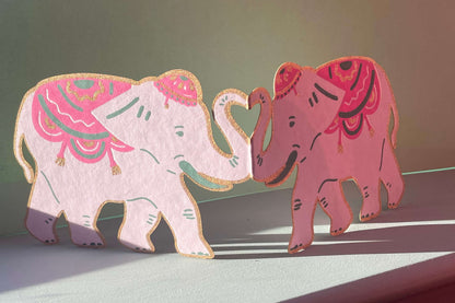 Two decorative elephants with pink and white patterns on a flat surface.
