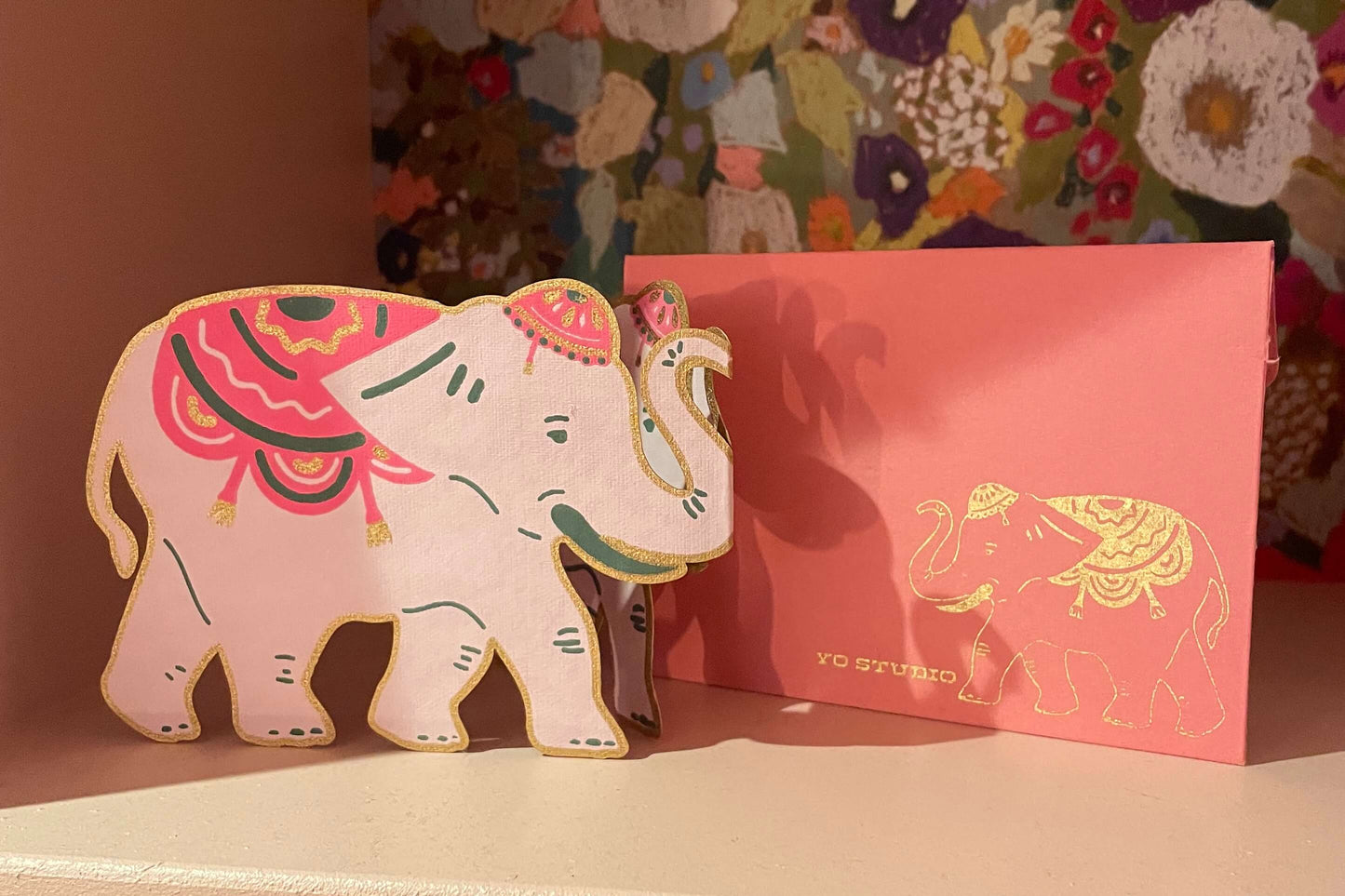 Decorative elephant figurine and envelope on a shelf with floral-patterned backdrop