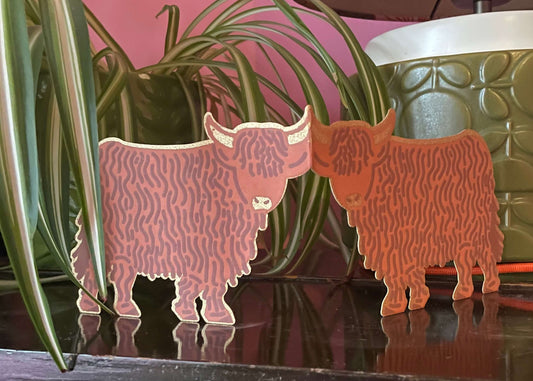 Two decorative cow figurines on a reflective surface with a floral-patterned lamp in the background.