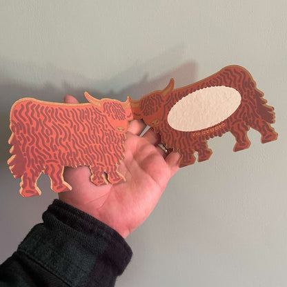 Hand holding inside of the highland cow against a plain background