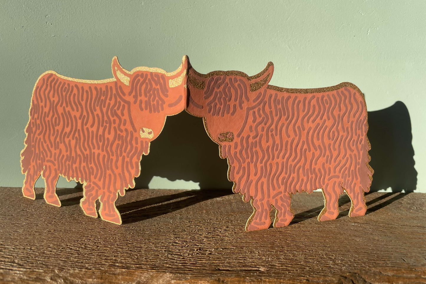 Highland cow card on a wooden surface with a light green background.