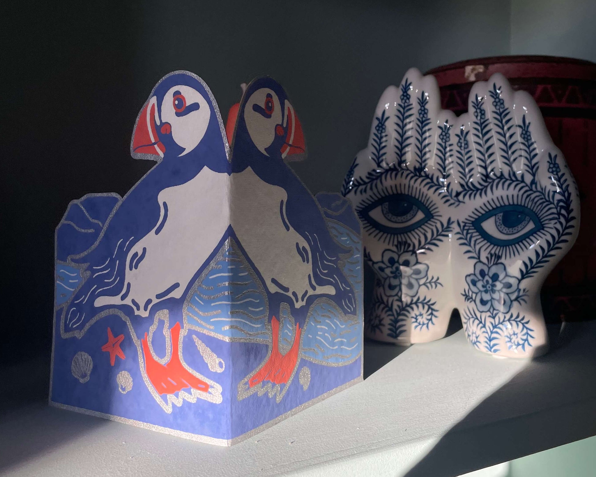 Decorative items on a shelf, including a puffin greetings card and a patterned vase.