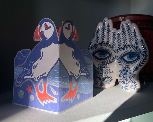 Decorative items on a shelf, including a puffin greetings card and a patterned vase.