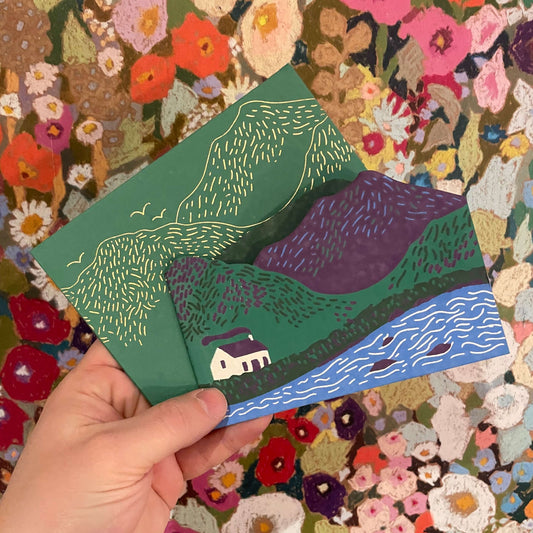 Hand holding a colorful landscape illustration against a floral background